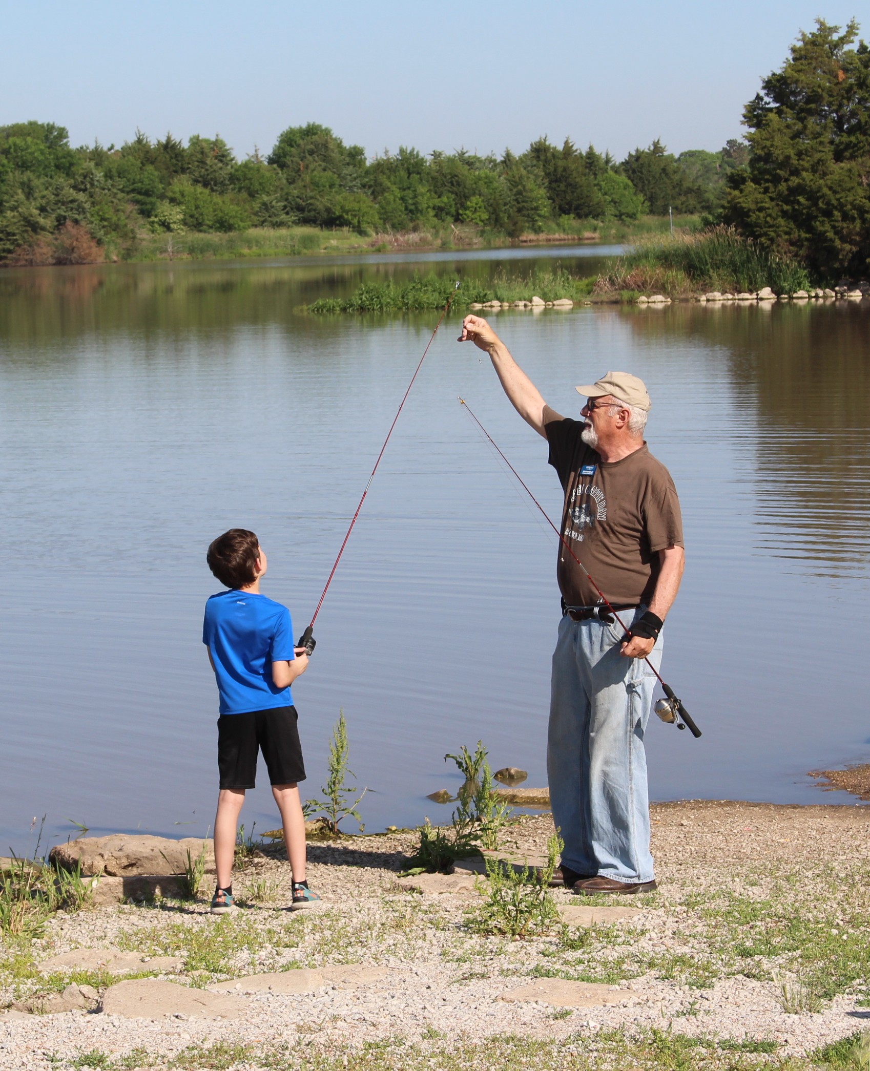 Fishing instructor helping young child with fishing pole.  Recharge Lake in the background.