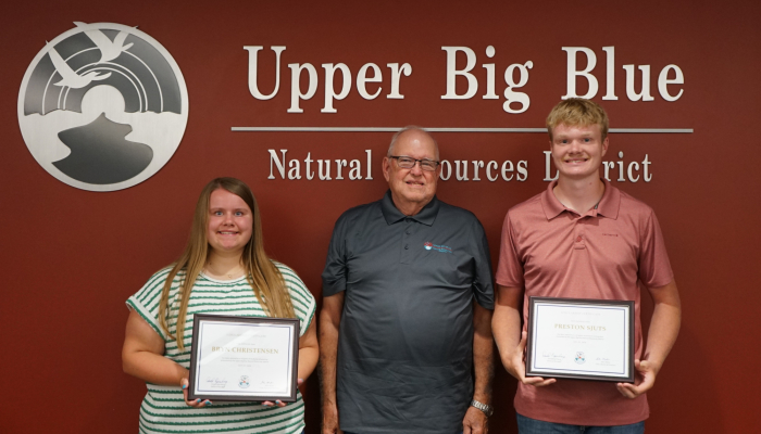 Bryn Christensen (left) and Preston Sjuts (right) hold their Burke Scholarship certificates and are pictures with Board Chair John Miller (center)