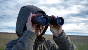 Person looking through binoculars at a birdwatching event.